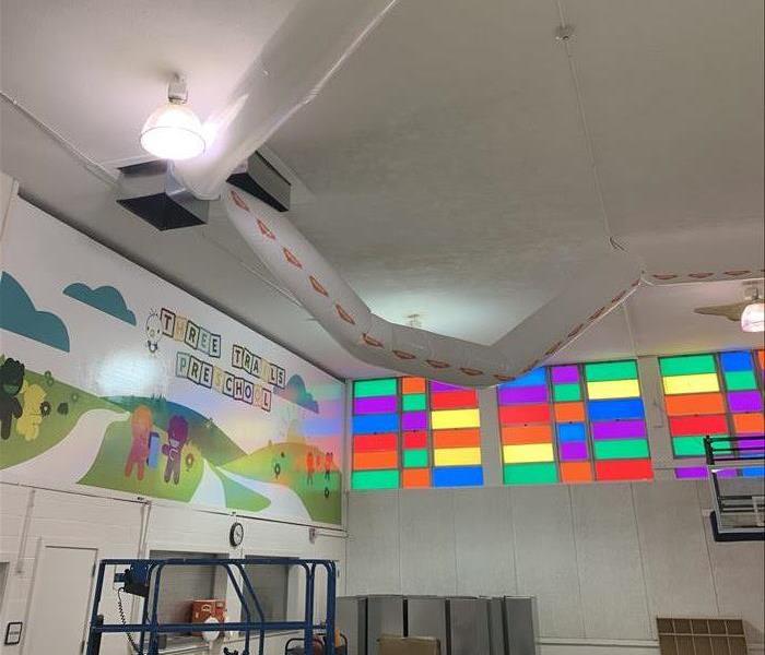 the upper part of the wall and ceiling of a colorful preschool with a large plastic tube set up through the vents